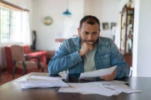 Unemployed person at table worrying over paperwork. Navigating Federal and Montana Unemployment Insurance in the COVID-19 Era - Worden Thane Legal Blog
