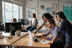 Three young employees gathered around a laptop at work.